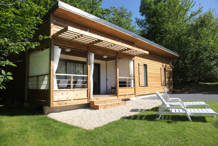 Chalet en bois du domaine Chalet en bois avec terrasse couverte et bains de soleil sur la pelouse, dans un environnement verdoyant près de Sarlat
