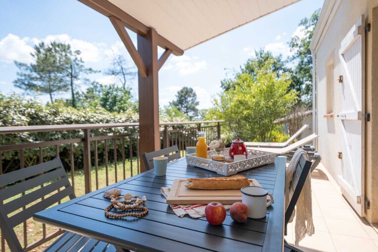 Petit-déjeuner en terrasse Petit-déjeuner dressé sur la terrasse ombragée d'un hébergement, face au jardin verdoyant du domaine